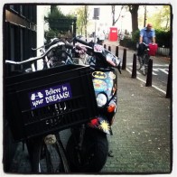 An Amsterdam bicycle and Vespa on the sidewalk together.